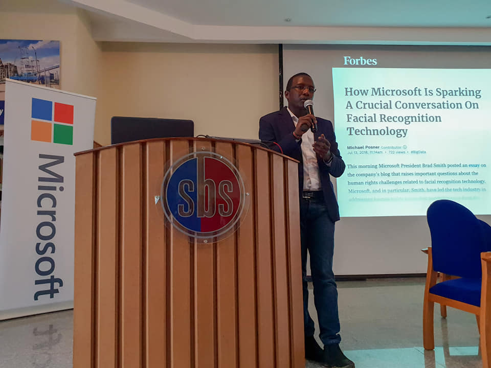 Somet Kipchilat speaking at a lectern, beside a slide on facial recognition technology